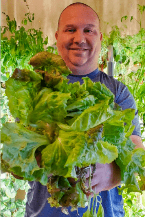 Man showcasing fresh lettuce in front of a Hydrogrowhub Home system.